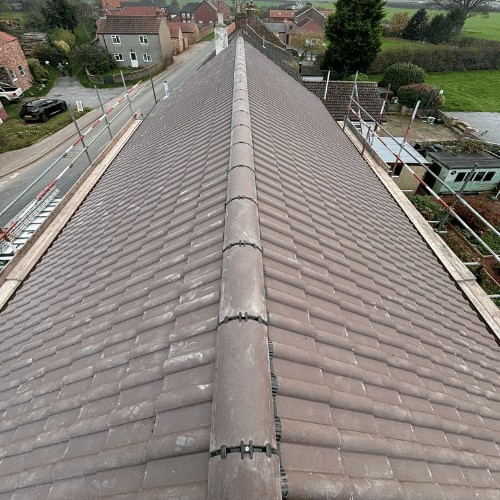Long run of new brown interlocking tiles viewed along the ridge from the scaffold