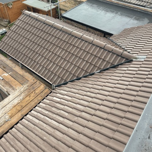 New tiled roof meeting a flat roof section, battens and scaffold visible